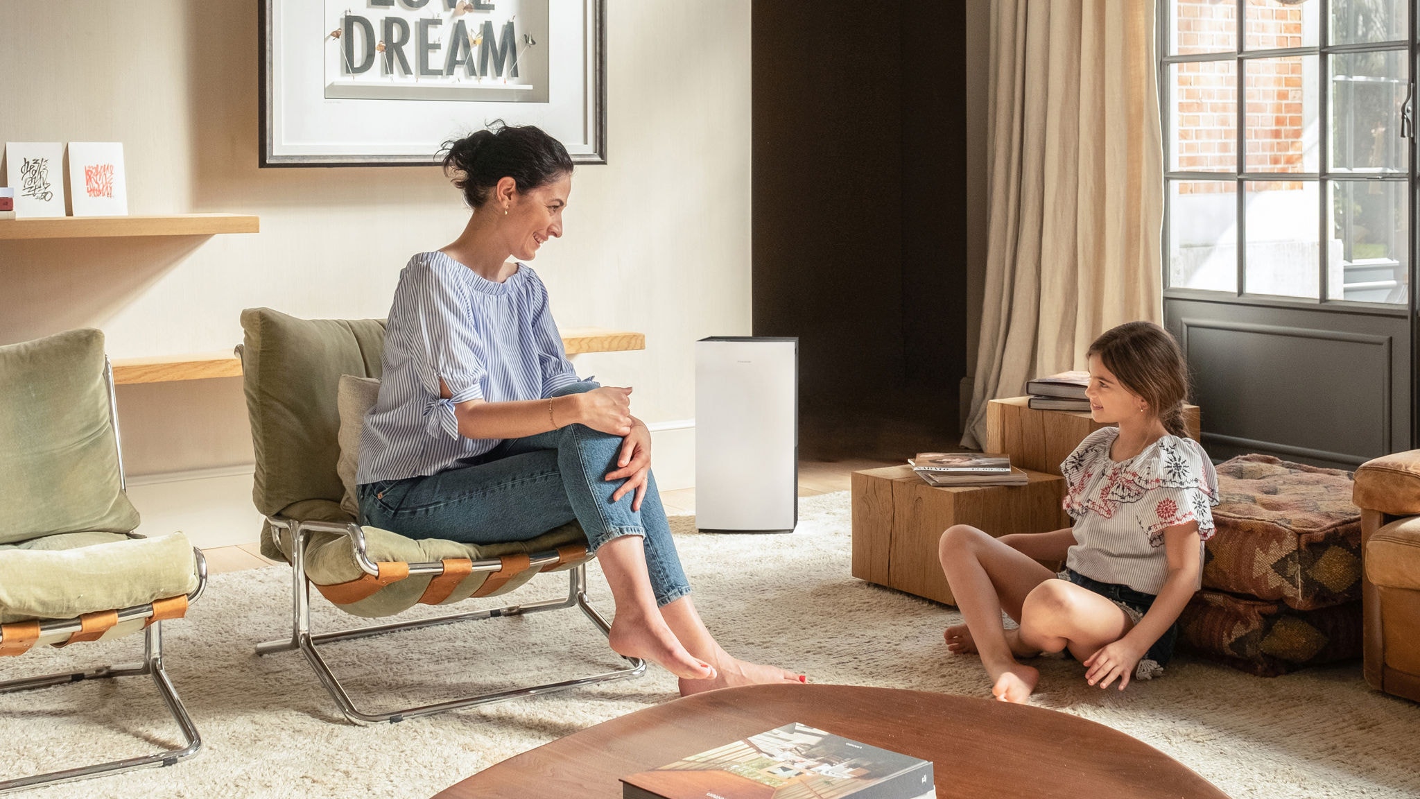 Mãe a falar alegremente com a sua filha pequena na sala que tem ar limpo graças a um purificador de ar Daikin